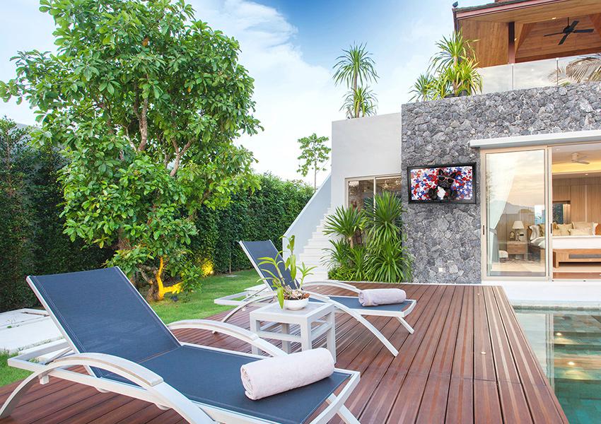 Backyard TV mounted to stone wall by sleek deck and pool