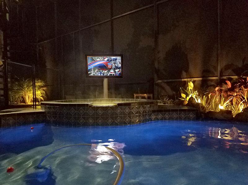 A weatherproof TV next to the pool, directly below the hot tub 