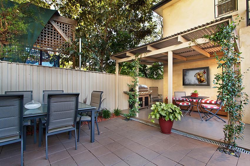 Lovely yellow awning with greenery and quaint dining spaces paired with an added wall mounted outdoor TV cabinet